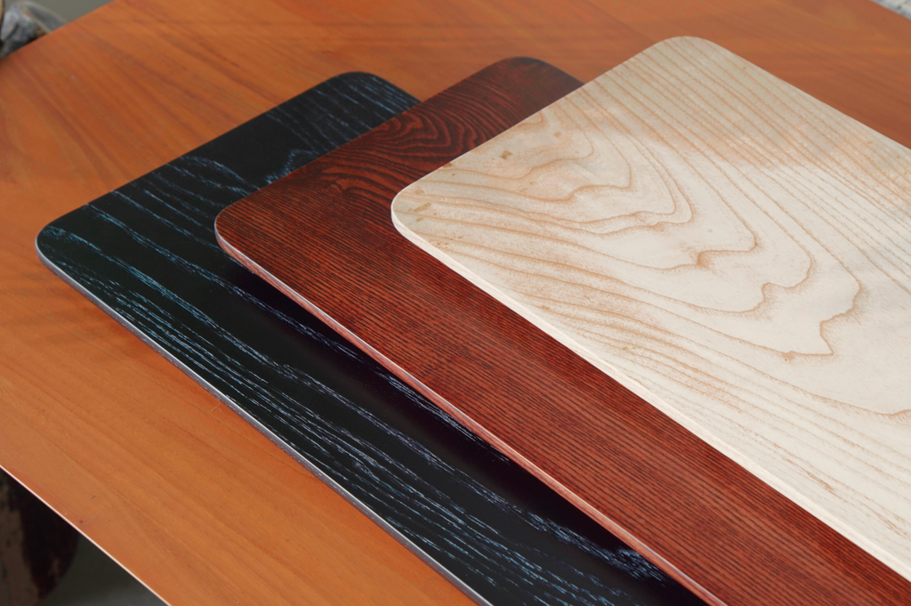 Three wooden desk shelf finishes in black, walnut, and natural oil of white ash wood on a wooden surface.